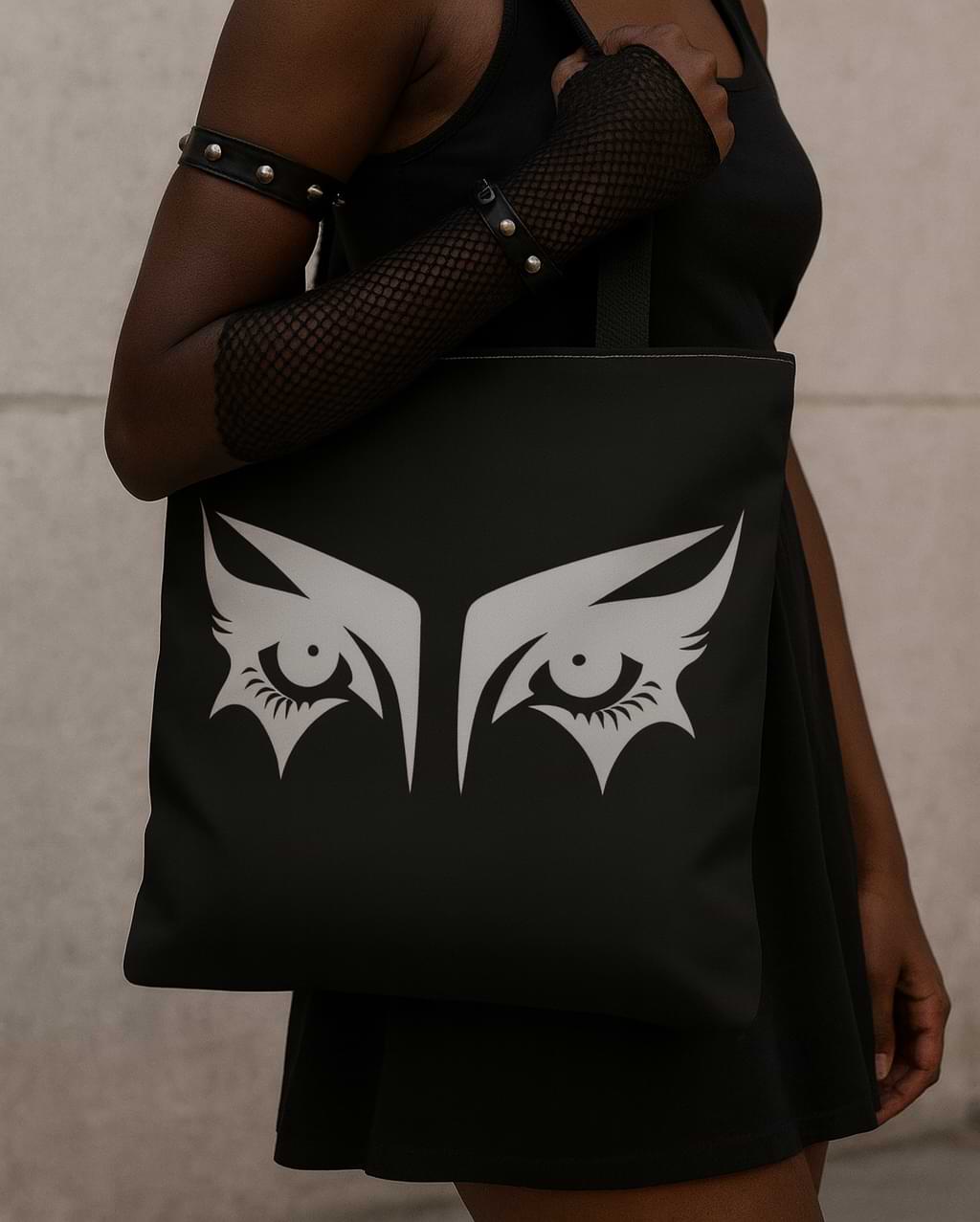 Goth girl carrying a gothic tote bag that has an illustration of trad goth makeup against a black background.