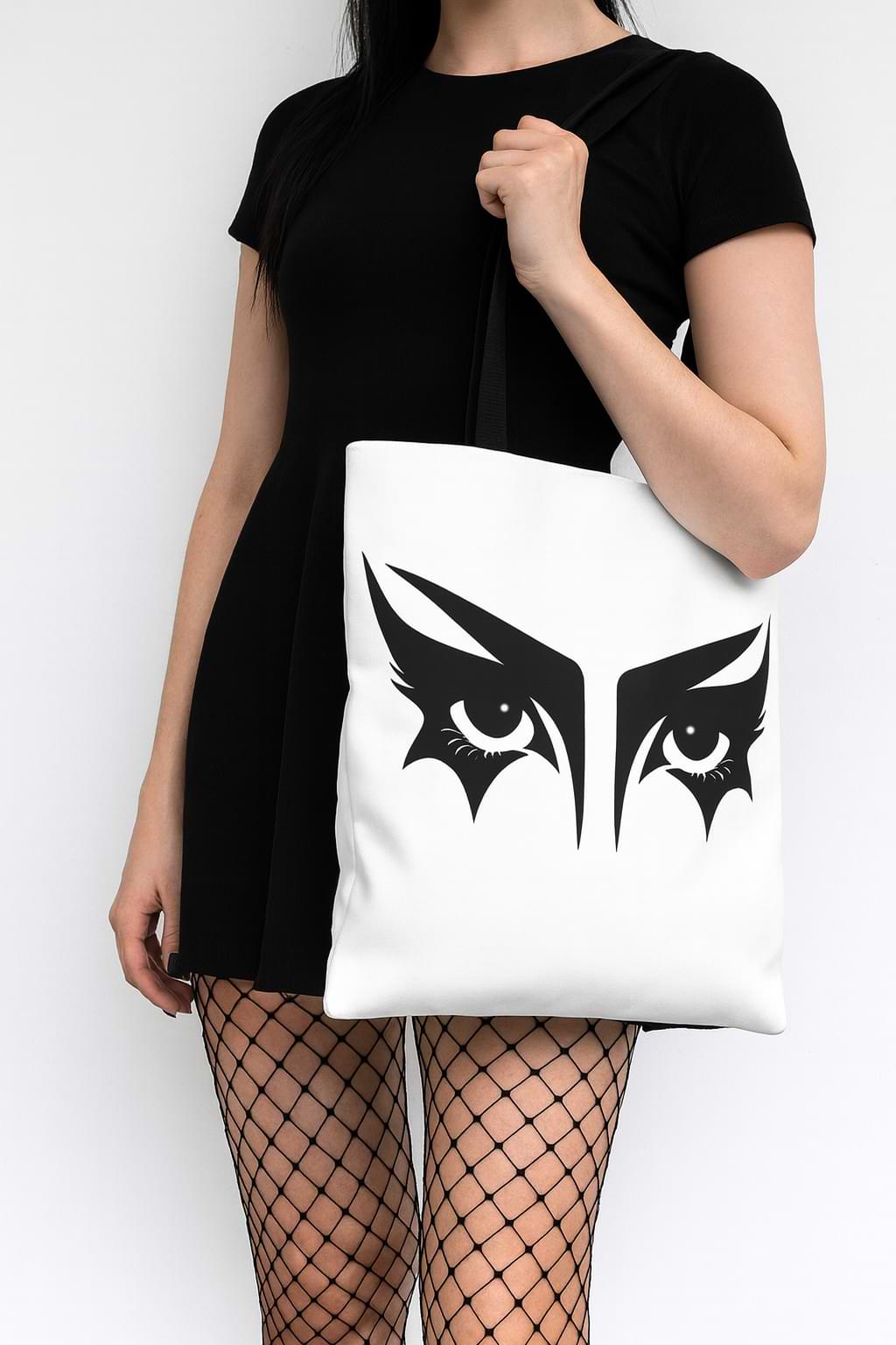 Goth girl carrying a gothic tote bag that has an illustration of trad goth makeup against a white background.