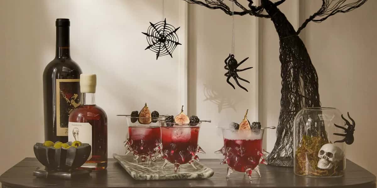 Dark gothic home bar styled with wine, black cocktails, skull decor, and spider web ornaments for Halloween.