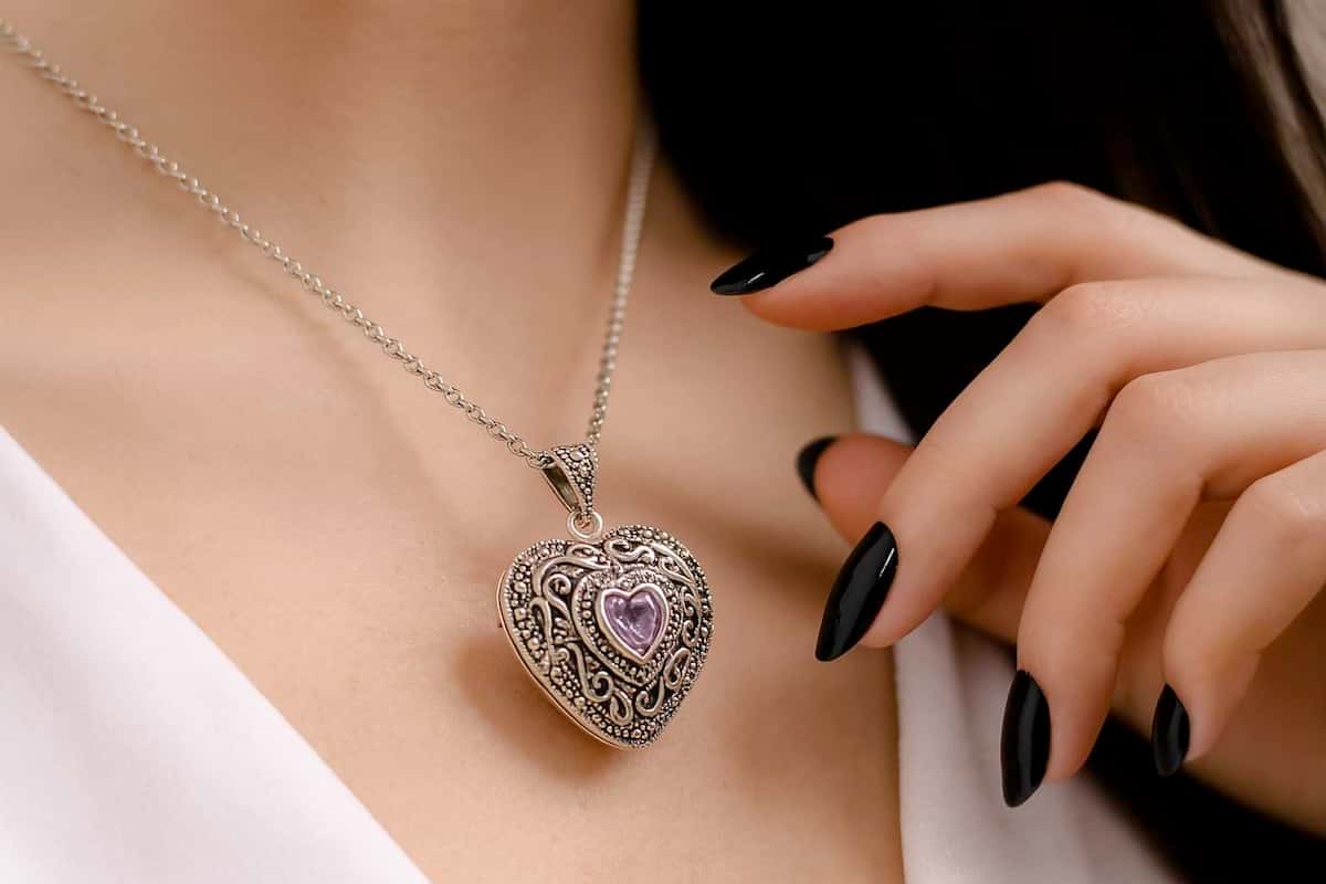 Close-up of a woman wearing a handmade sterling silver heart locket with amethyst crystal, hand reaching toward it.