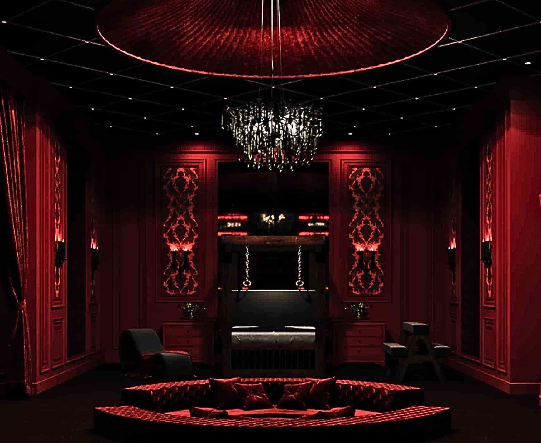 Goth sex dungeon design complete with an ornate black chandelier, red velvet couches and curtaints, plush red walls, and liberator BDSM furniture.