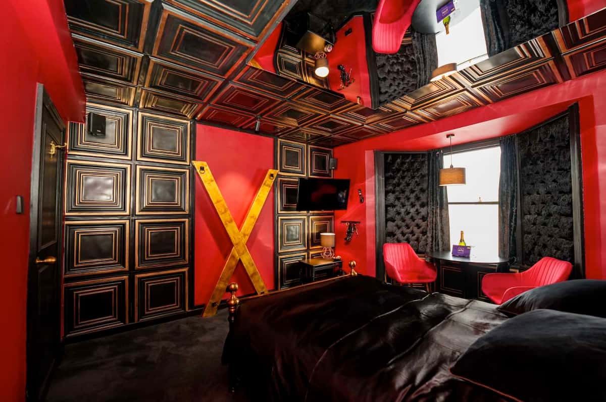 Luxurious BDSM dungeon with red and black decor, St. Andrew’s Cross, leather bedding, and mirrored ceiling.
