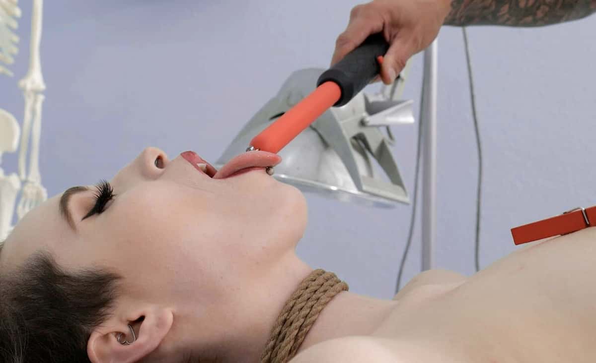 A woman in rope bondage sticking out her tongue to receive an electro stimulation shock from a violet wand