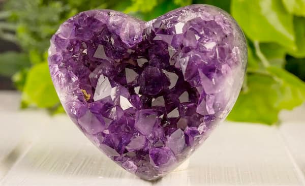 Amethyst heart crystal cluster propped up on a stand against a natural background