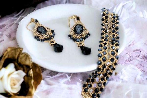 Gold and black Swarovski beaded bracelet with matching cameo earrings on white dish