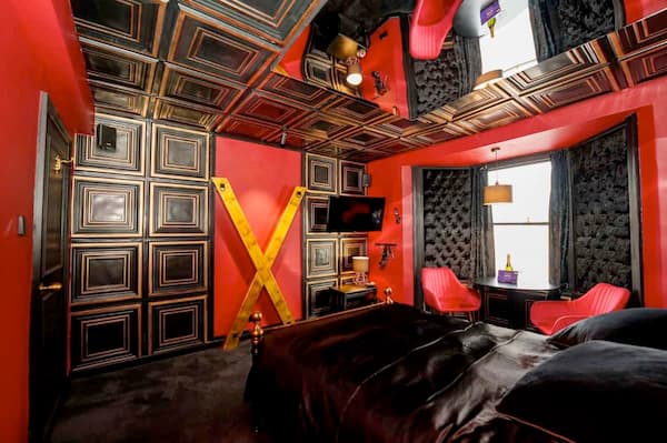 Luxurious BDSM dungeon with red and black decor, St. Andrew’s Cross, leather bedding, and mirrored ceiling.