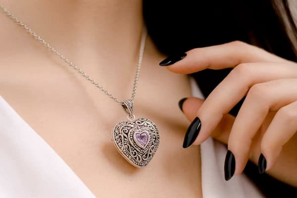 Close-up of a woman wearing a handmade sterling silver heart locket with amethyst crystal, hand reaching toward it.