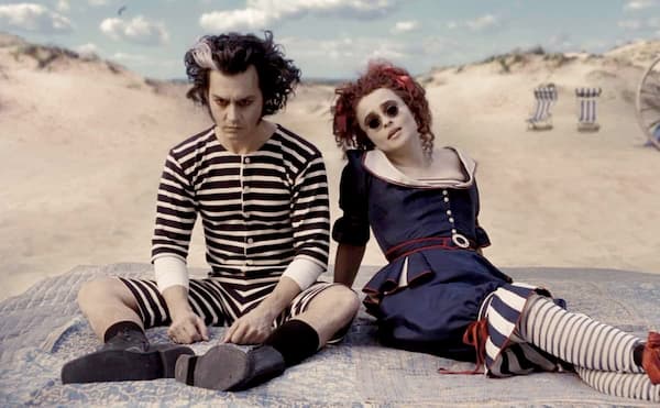 Sweeney Todd and Mrs. Lovett sit on a beach in Victorian striped swimwear, embodying moody beach goth aesthetic.