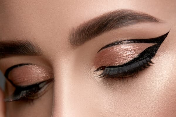 Close-up of graphic eyeliner look with sharp double wings and rose gold shimmer eyeshadow, showcasing precise application with the best drugstore eyeliner.
