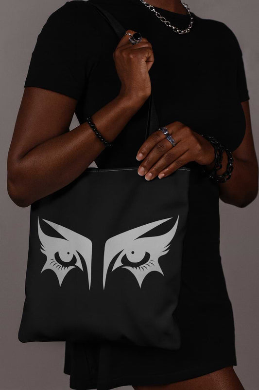 Goth girl carrying a gothic tote bag that has an illustration of trad goth makeup against a black background.