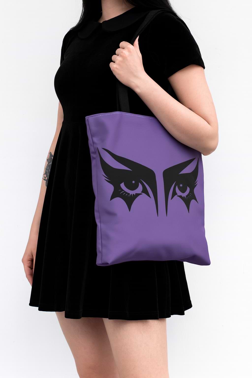 Goth girl carrying a gothic tote bag that has an illustration of trad goth makeup against a lilac background.